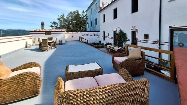 A rooftop terrace with wicker furniture, a dining area, and a white building with a sign.