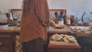 A person in a kitchen with wooden countertops, a basket on the wall, and various kitchen utensils.
