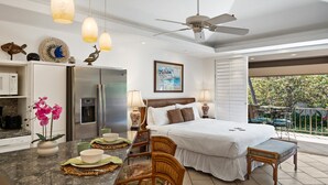 Ein modernes Hotelzimmer mit einem großen Bett, einer Essecke, einer Küche und einem Balkon mit Blick auf den Garten.