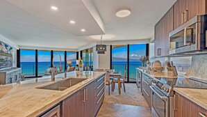 A modern kitchen with a large island, stainless steel appliances, and a view of the ocean. - Beachfront 2BR condo w stunning ocean views - Kaanapali Shores 702 (Lahaina)
