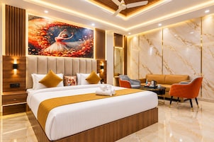Una habitación de hotel moderna con una cama grande, una zona de estar con sofá y sillones, y un mural decorativo en la pared.