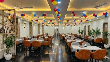 Een ruime balzaal met meerdere tafels en stoelen, plafondventilatoren en decoratieve ballonnen.