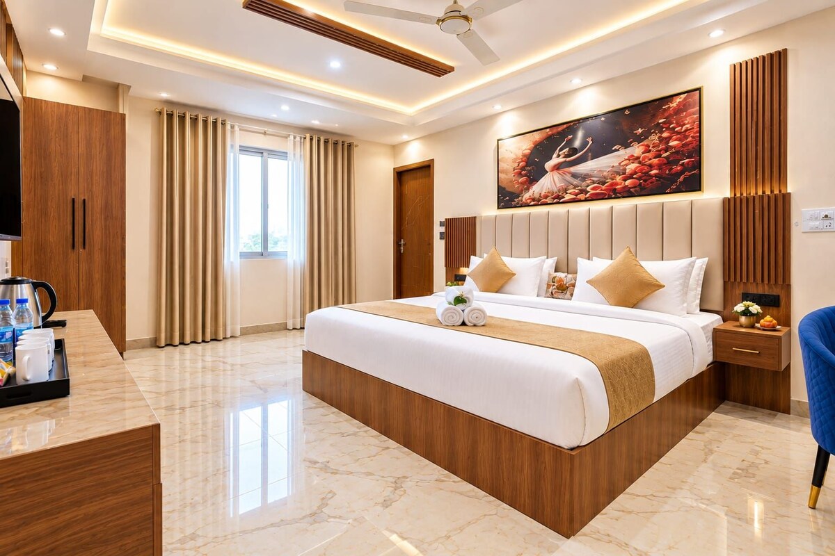 A modern hotel room with a large bed, a desk with a coffee maker, and a large window with curtains.