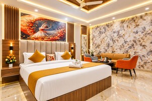 Een moderne hotelkamer met een groot bed, een zithoek met een bank en stoelen, een decoratieve wand met een bloemenpatroon en een plafondventilator.