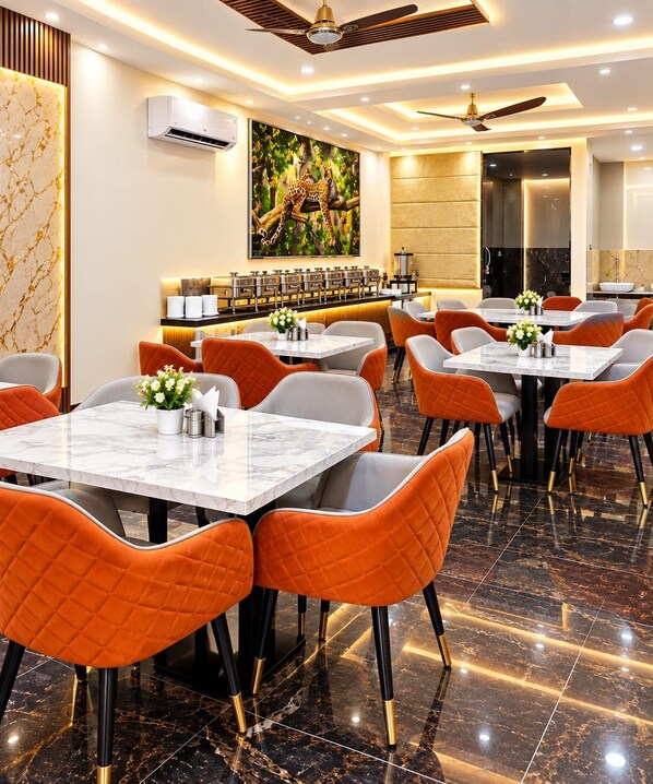 A modern restaurant interior with marble flooring, orange and grey upholstered chairs, and a central dining area with tables. - Hotel NS Near Delhi Airport (New Delhi)