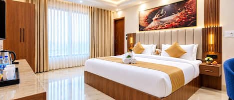 A modern hotel room with a large bed, a flat-screen TV, a desk with a coffee maker, and a large window with curtains.