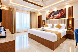 Een moderne hotelkamer met een groot bed, een flatscreen-tv, een bureau met een koffiezetapparaat en een groot raam met gordijnen.
