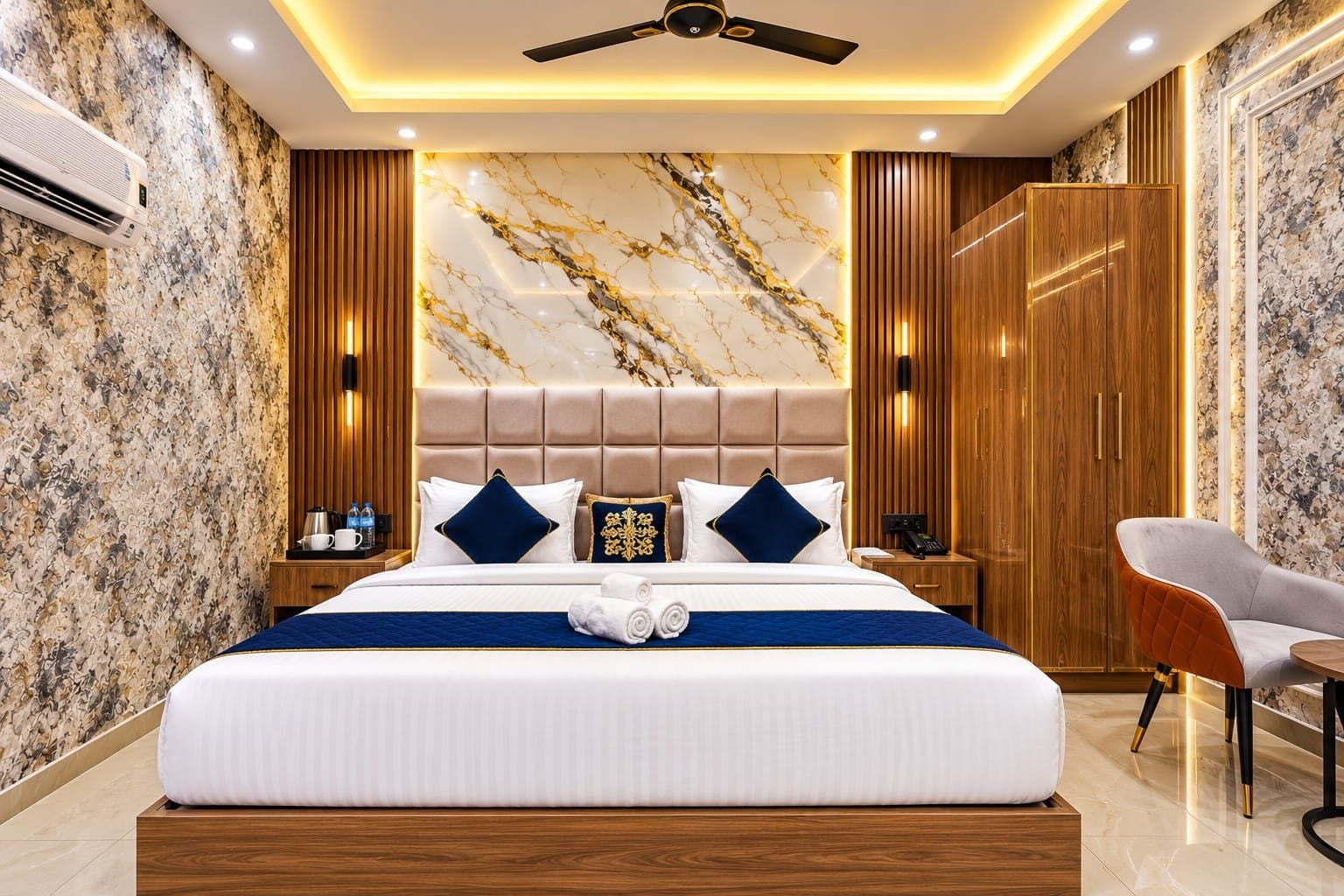 A modern hotel room with a marble-patterned wall, a large bed with a headboard, wooden furniture, and a ceiling fan.