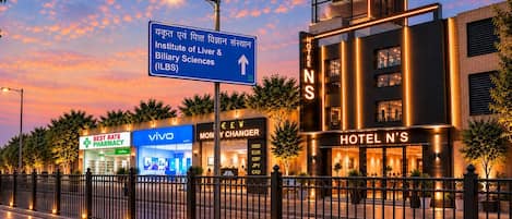 A modern hotel with a prominent sign, a pharmacy, and a Vivo store.