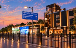 A modern hotel with a prominent sign, a pharmacy, and a Vivo store. - Hotel NS Near Delhi Airport (New Delhi)