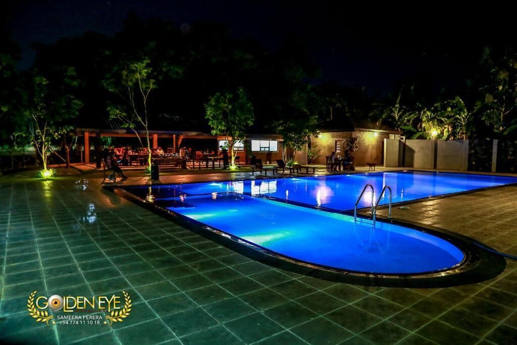 A nighttime swimming pool area with a covered seating area and a building in the background.