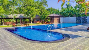 A swimming pool with a tiled deck, surrounded by trees and a covered seating area. - Doola River Edge (Udawalawa)