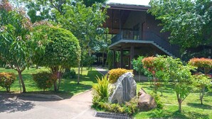 A building with a covered outdoor area, surrounded by well-maintained greenery and a paved pathway. - Doola River Edge (Udawalawa)