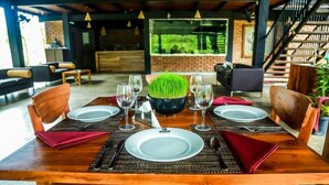 A wooden dining table set with white plates, red napkins, and wine glasses, surrounded by wooden chairs. - Doola River Edge (Udawalawa)