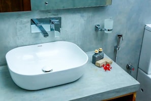 A modern bathroom with a large white sink, a mirror, a handheld showerhead, and a soap dispenser. - Doola River Edge (Udawalawa)