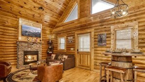 A log cabin interior with a stone fireplace, wooden furniture, and a dining area. - Majestic Bear Retreat, WIFI, Free Attraction ticket, Hot Tub (Pigeon Forge)