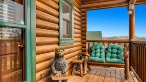 A log cabin with a wooden porch, a welcome sign, a bear statue, and a green chair. - Majestic Bear Retreat, WIFI, Free Attraction ticket, Hot Tub (Pigeon Forge)