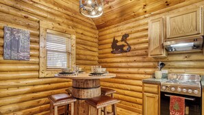 A cozy log cabin interior with a wooden dining table, bar stools, a stove, and a window with blinds. - Majestic Bear Retreat, WIFI, Free Attraction ticket, Hot Tub (Pigeon Forge)