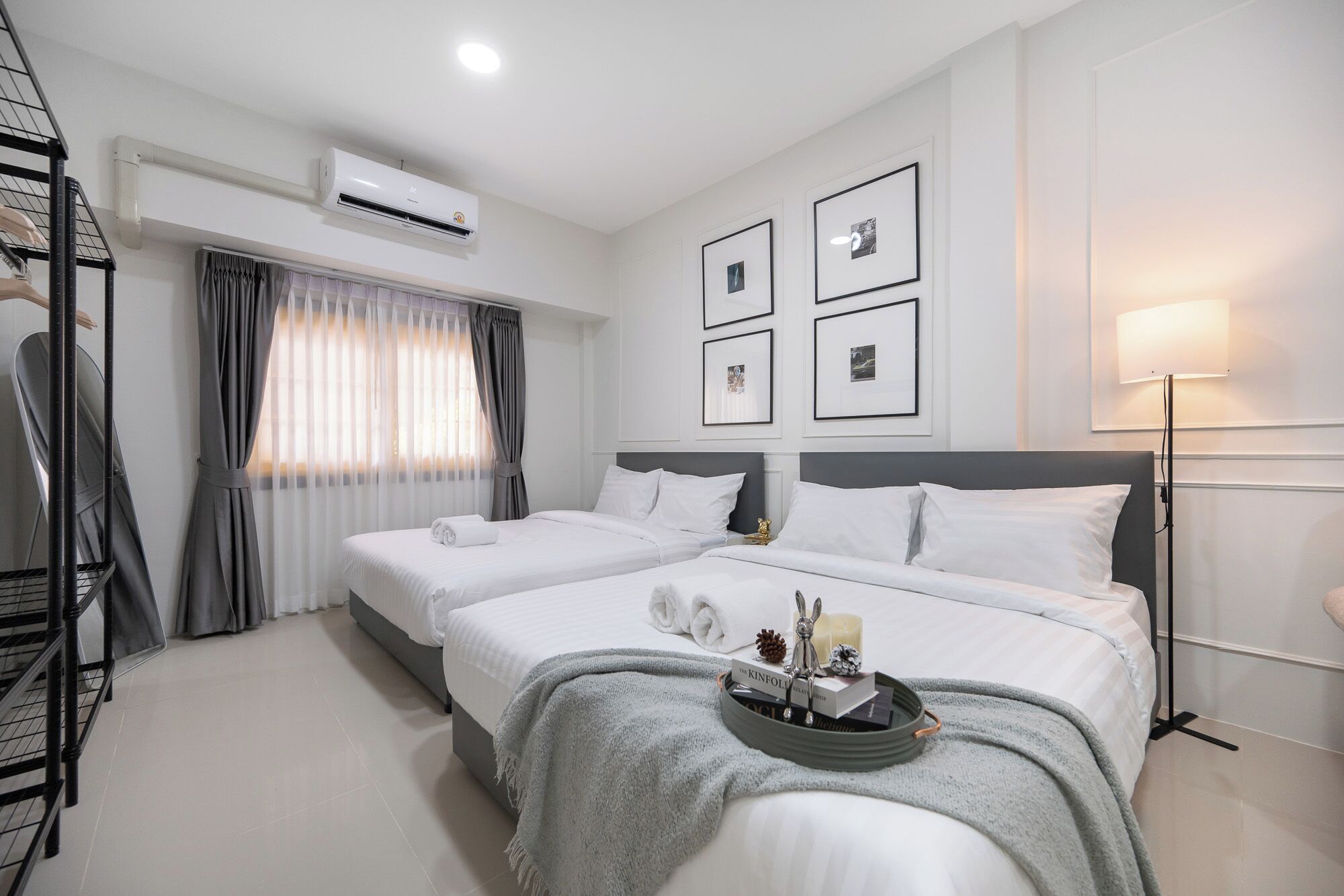 Een hotelkamer met twee bedden, een grijs hoofdeinde, een nachtkastje met een lamp en een wandairconditioner.