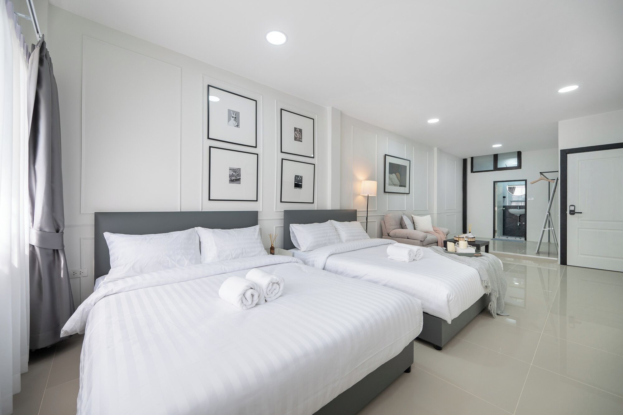 A modern hotel room with two large beds, a sofa, a small table with a lamp, and framed pictures on the wall.