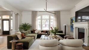 Een ruime woonkamer met een groene bank, een bijzettafeltje en een open haard.