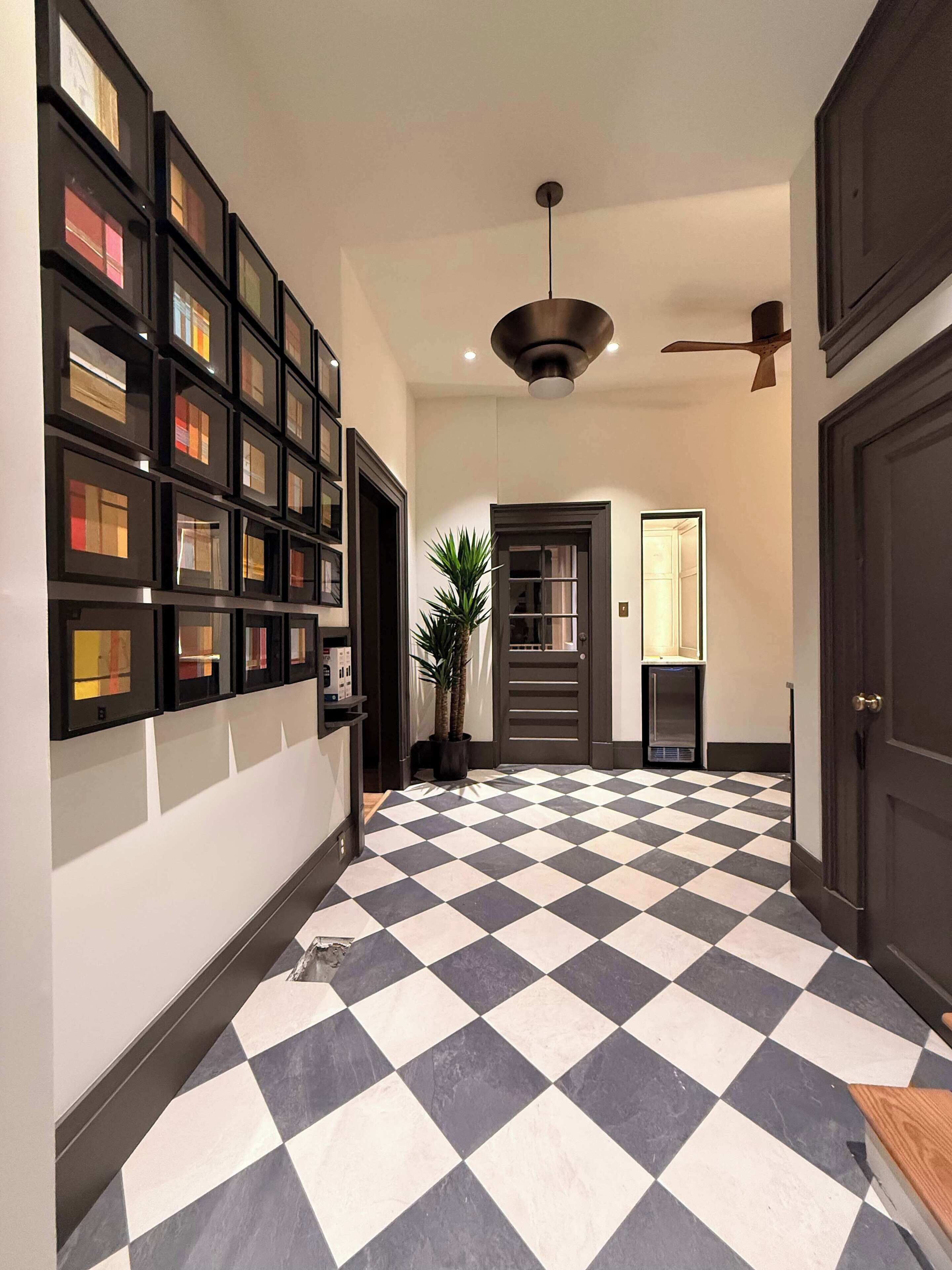 Un couloir avec un sol à carreaux, un ventilateur de plafond et un mur recouvert de tableaux encadrés.