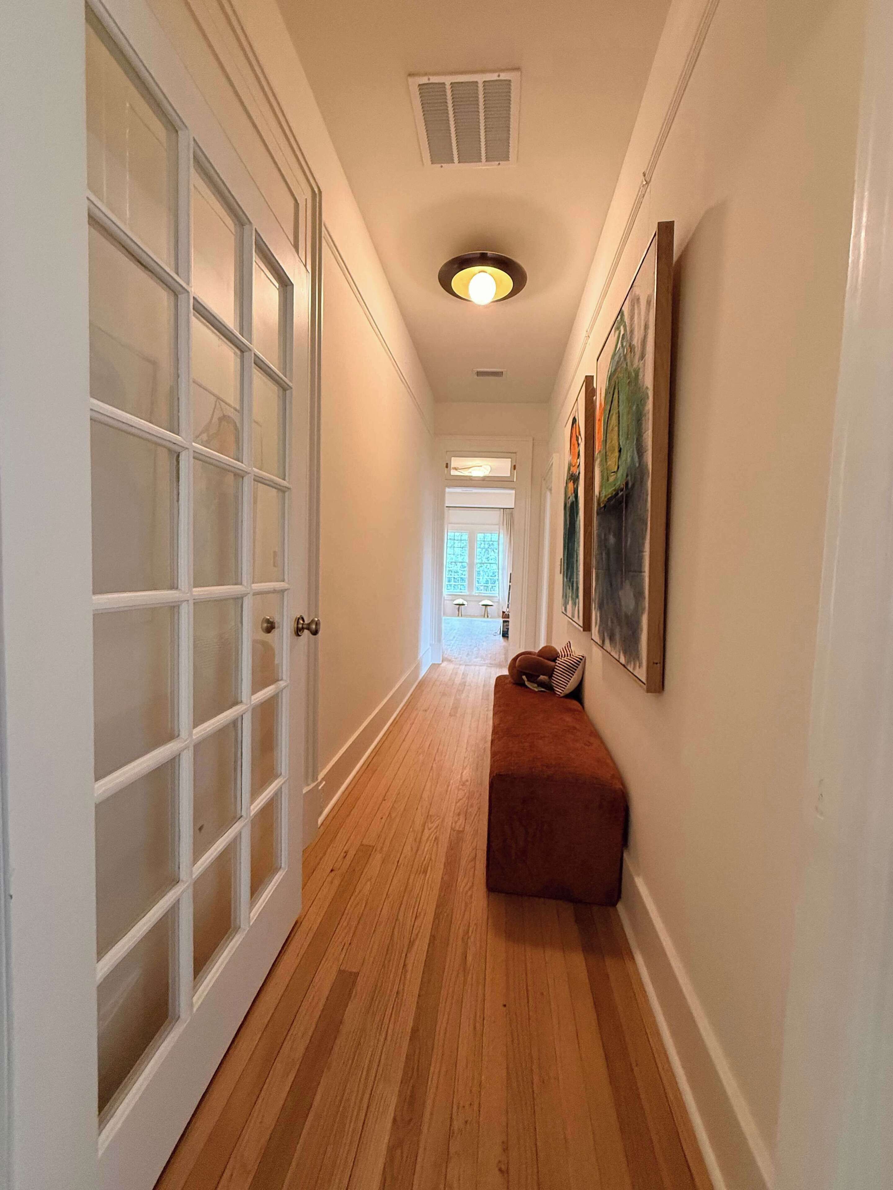 A hallway with a wooden floor, a bench, and a door with frosted glass panels.