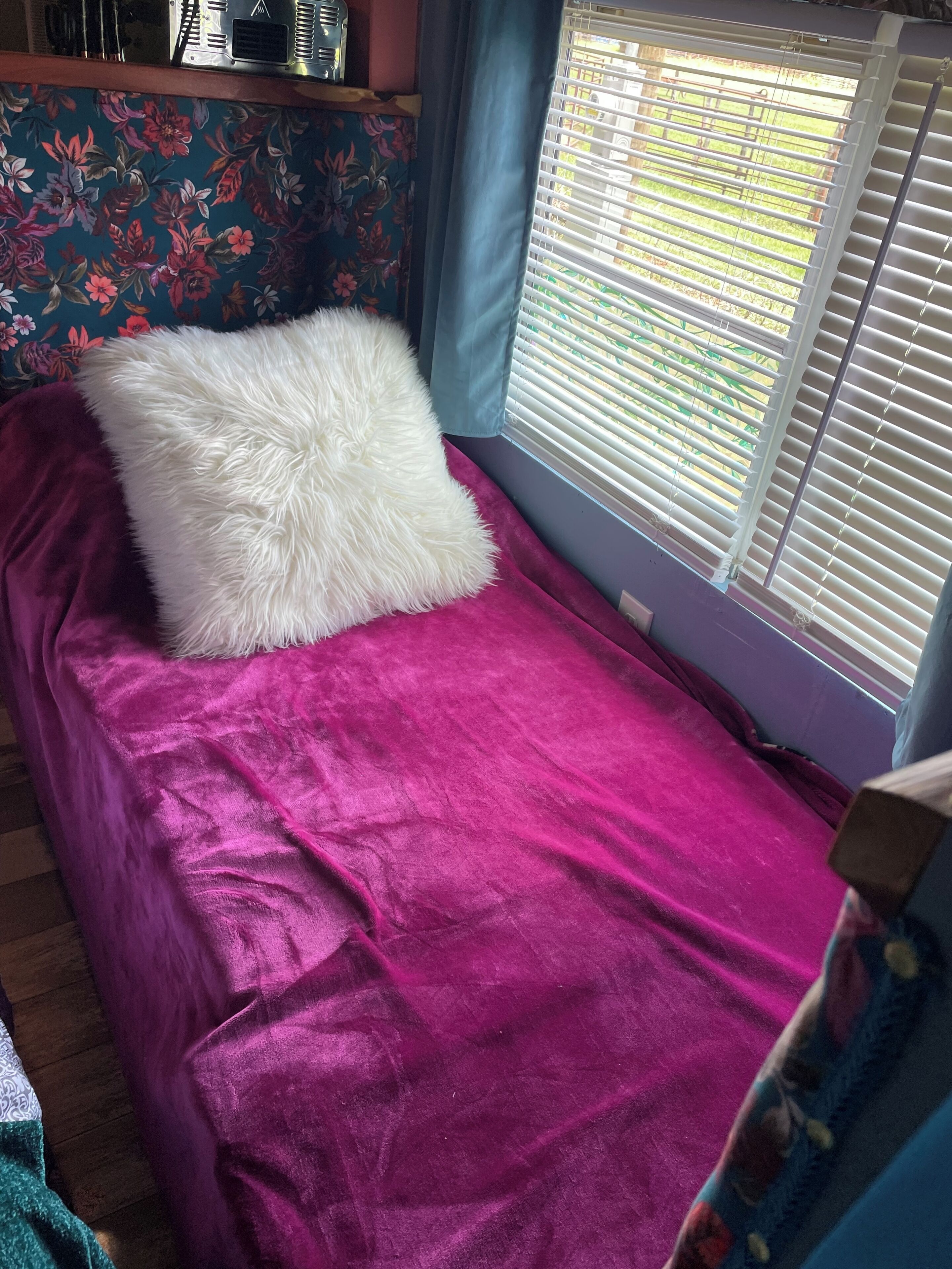 A small bed with a white fluffy pillow and a purple bedspread.