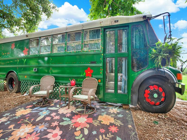 Un autobus vert avec des sièges en osier et une table, garé sur un tapis fleuri.