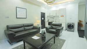 Een moderne woonkamer met een bank, fauteuils en een salontafel. Er is een keuken met apparatuur en een wasmachine.