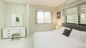 Een slaapkamer met een bed, een dressoir, een spiegel, een raam met jaloezieën en een airconditioner.