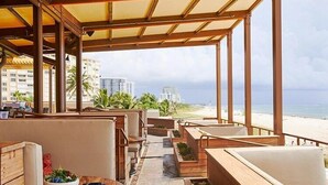 Un restaurante frente a la playa con terraza, vista a la playa y al océano, y palmeras.