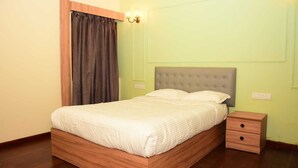 A bedroom with a wooden bed frame, a grey upholstered headboard, a bedside table, and a nightstand. - Whispering Pines (Ootacamund)
