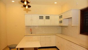 A kitchen with white cabinets, a white countertop, and a wooden table with stools. - Whispering Pines (Ootacamund)