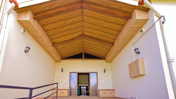 A covered outdoor area with a wooden ceiling, a metal railing, and a door leading to an interior space. - Whispering Pines (Ootacamund)