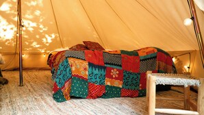 A tent with a colorful quilted bedspread and a wooden chair. - Hurtwood Hideout (Dorking)