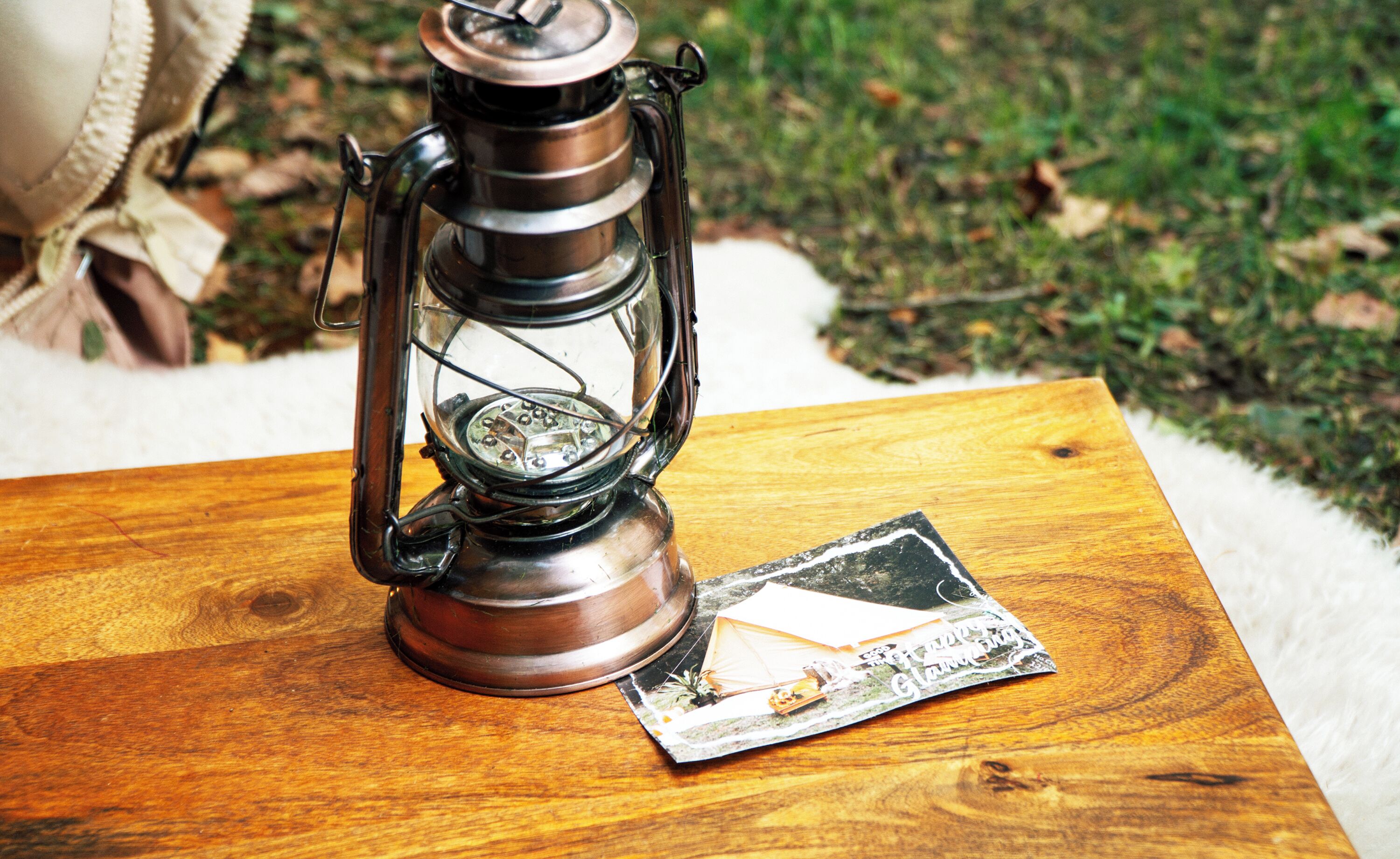 A vintage lantern on a wooden table with a postcard beside it.