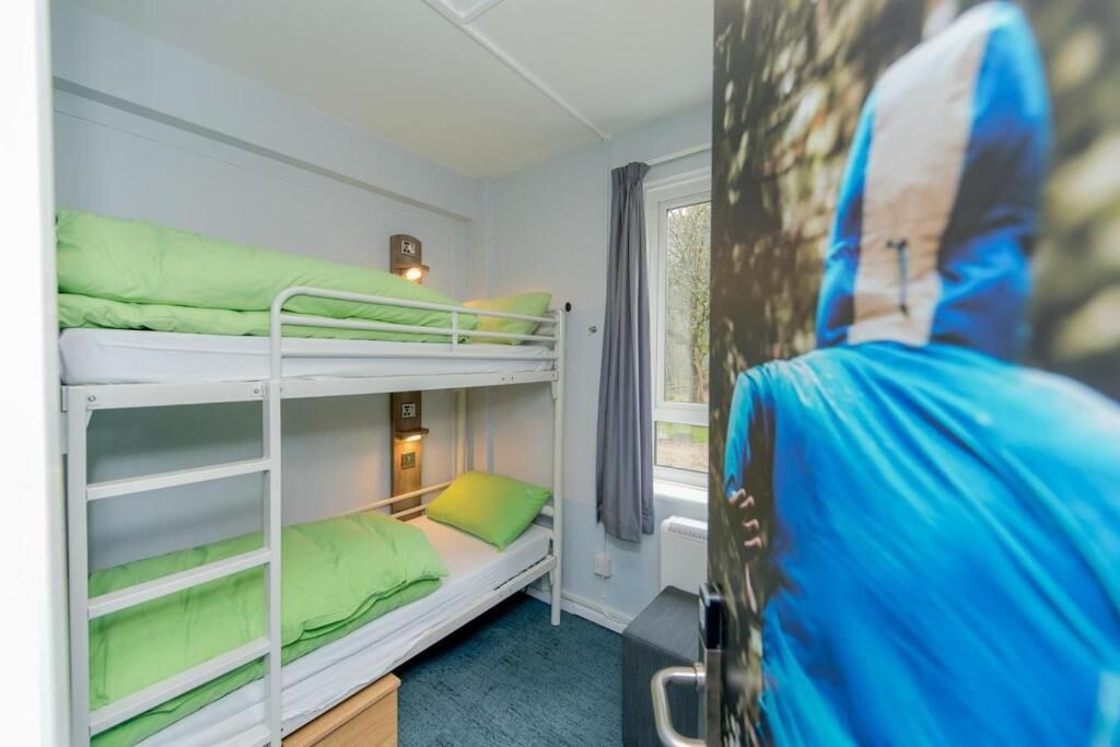 Une chambre avec un lit superposé, une fenêtre, une table de chevet et une affiche accrochée au mur.