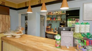 A bakery counter with a sign apologizing for a missed customer, a computer, and shelves stocked with snacks and beverages. - Hurtwood Hideout (Dorking)