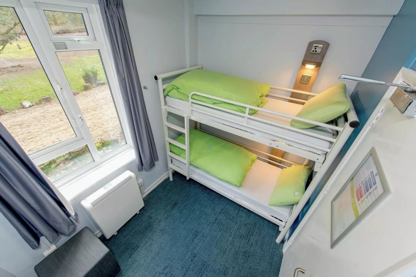 A bunk bed room with a window, a radiator, and a small table.