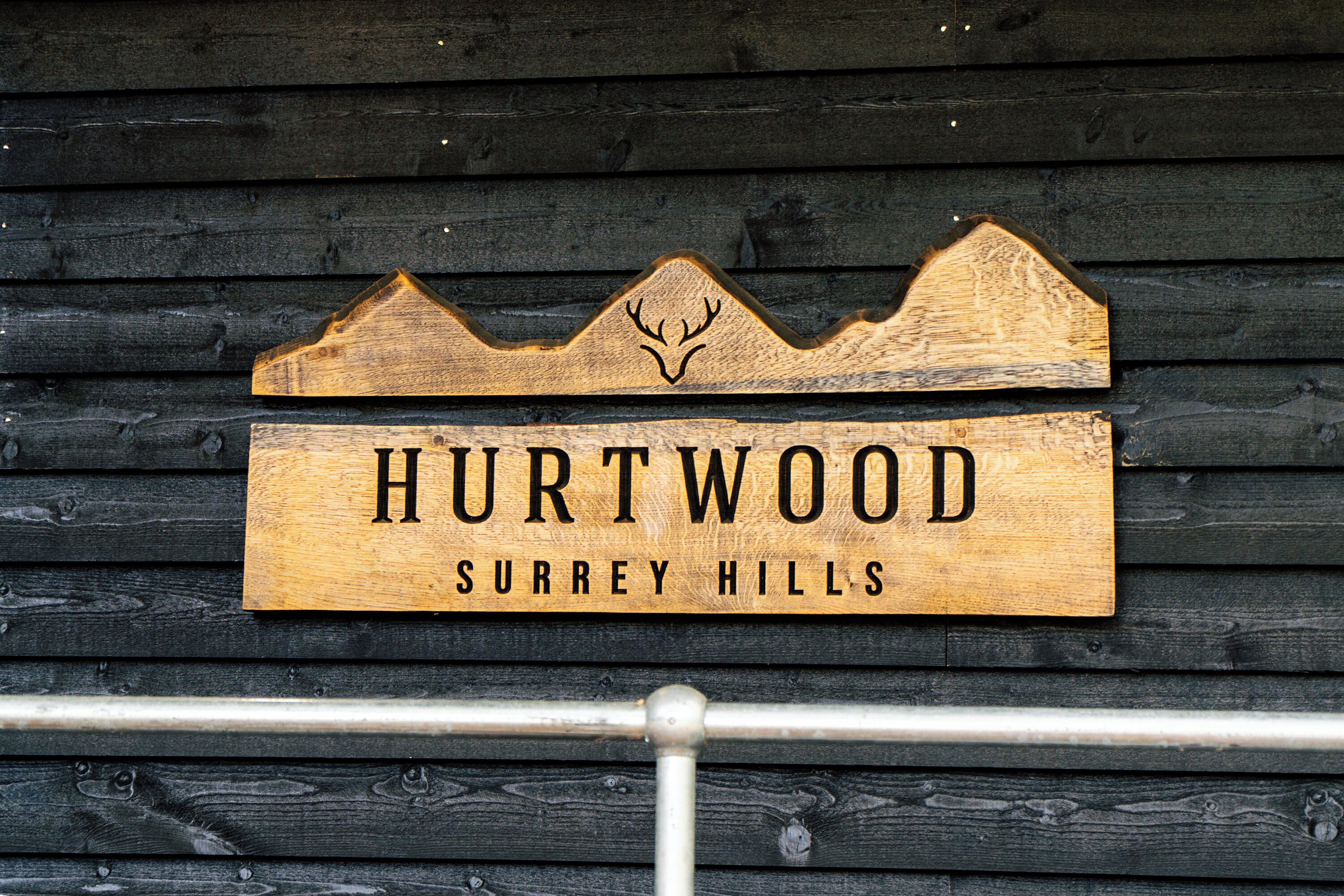 A wooden sign with the text "HURTWOOD" and "SURREY HILLS" against a wooden background.