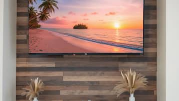 A flat-screen TV mounted on a wooden wall with a sunset beach scene. Below the TV, there is a gray console with two decorative vases.