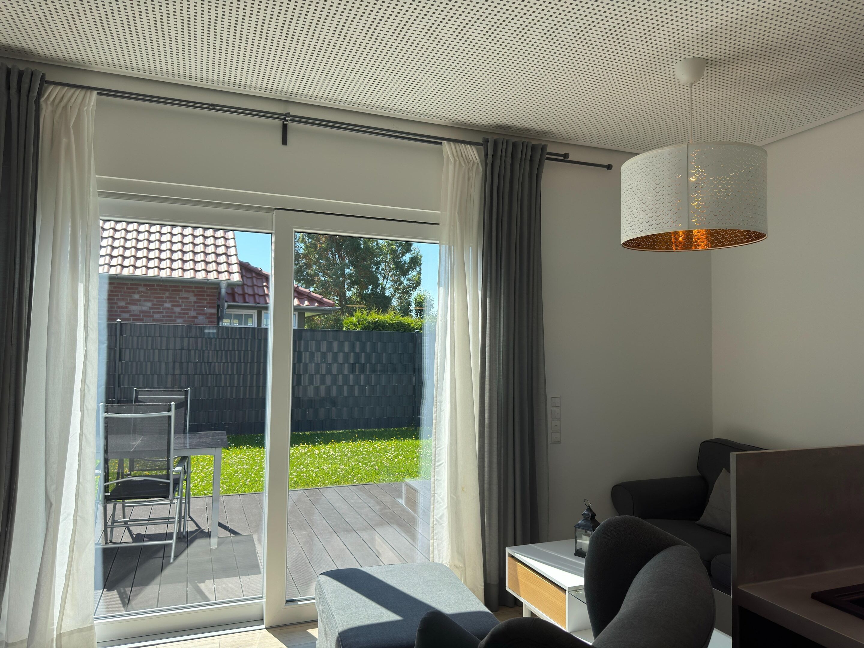 A modern room with a sliding glass door leading to a deck, a sofa, a small table, and a hanging light fixture.