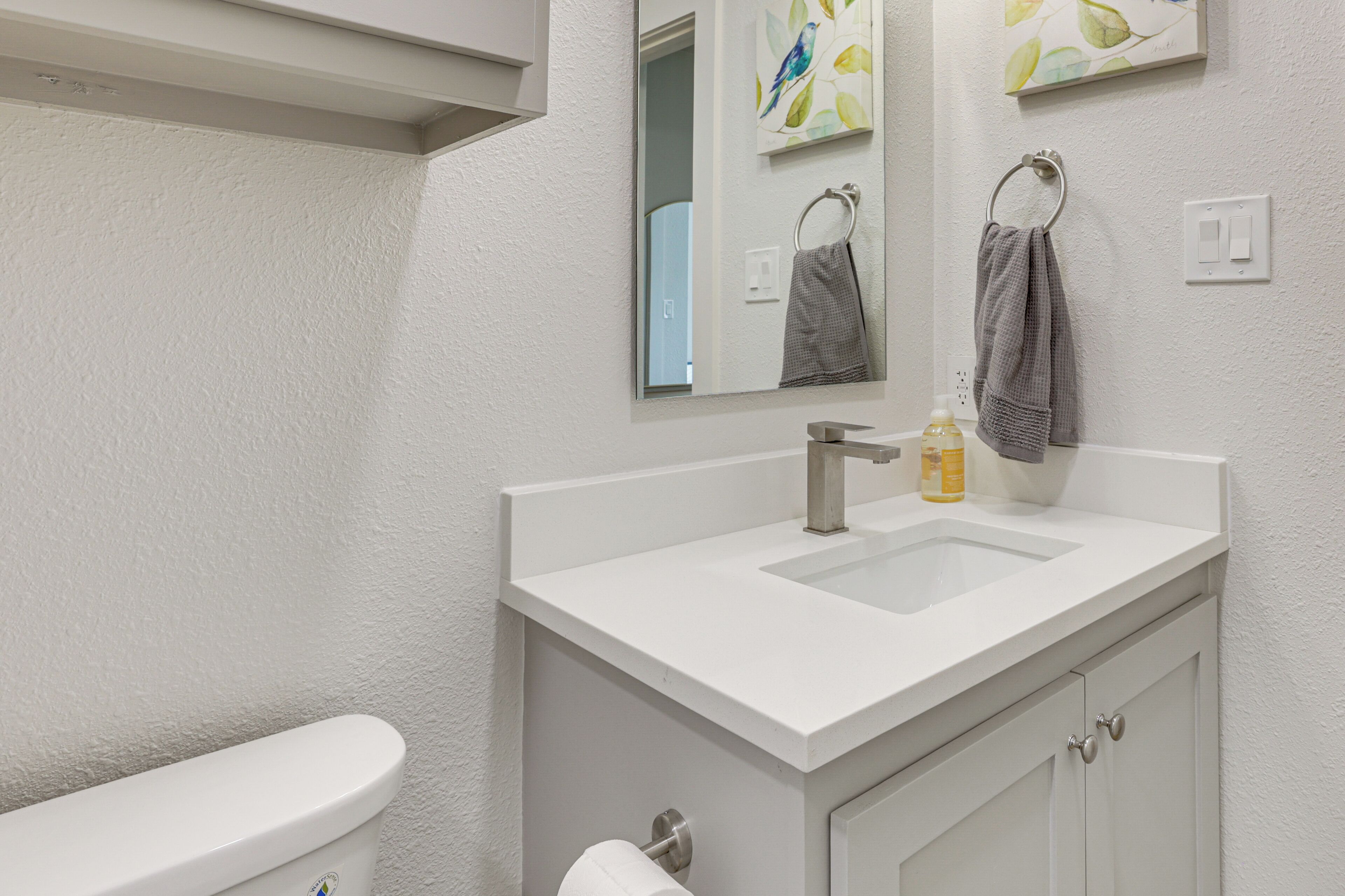 A bathroom with a white sink, a toilet, and a mirror. There are towels hanging on the wall and a soap dispenser on the sink.