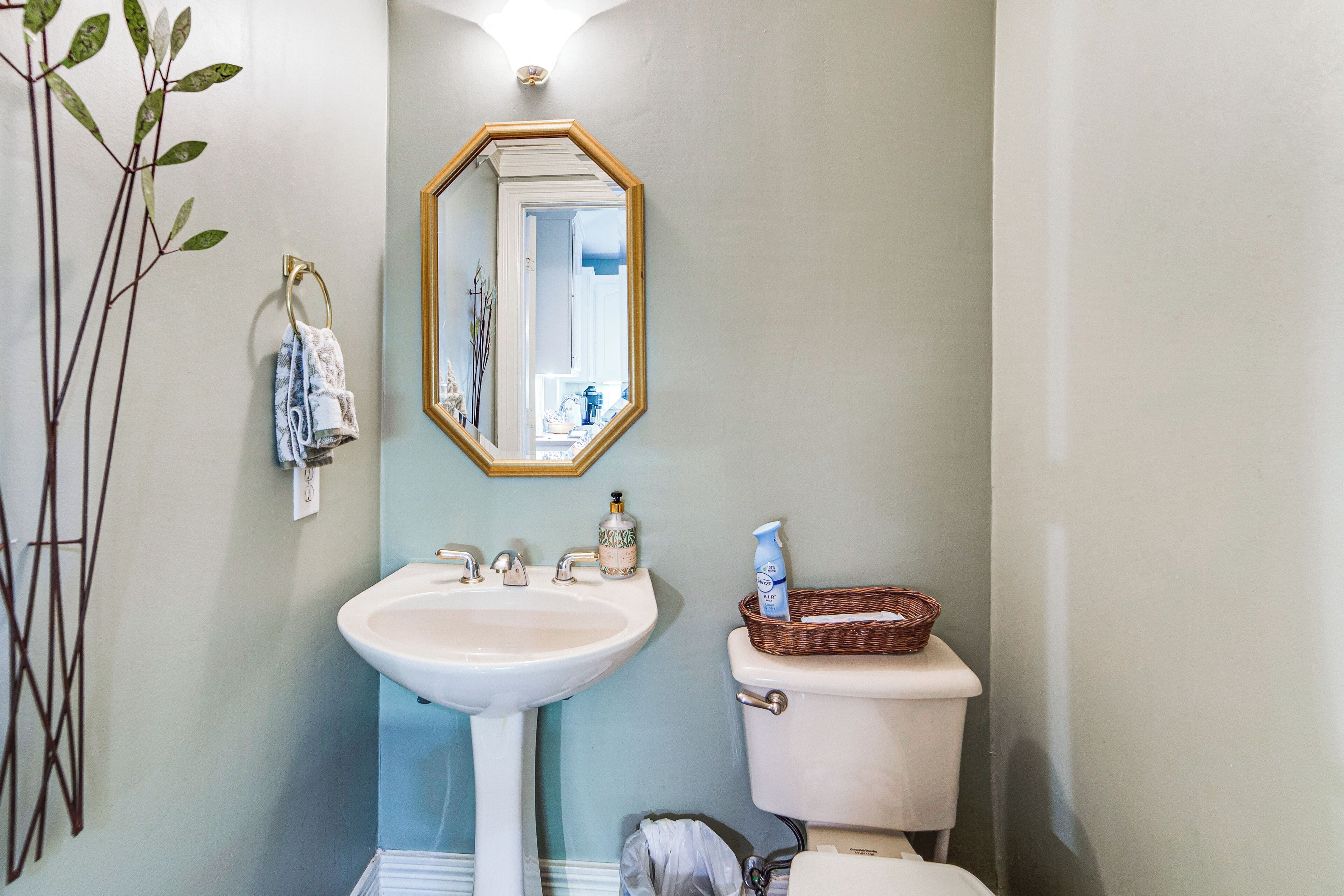 A bathroom with a white sink, a mirror with a gold frame, a toilet, and a wicker basket on the toilet.
