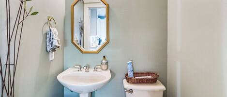 A bathroom with a white sink, a mirror with a gold frame, a toilet, and a wicker basket on the toilet.