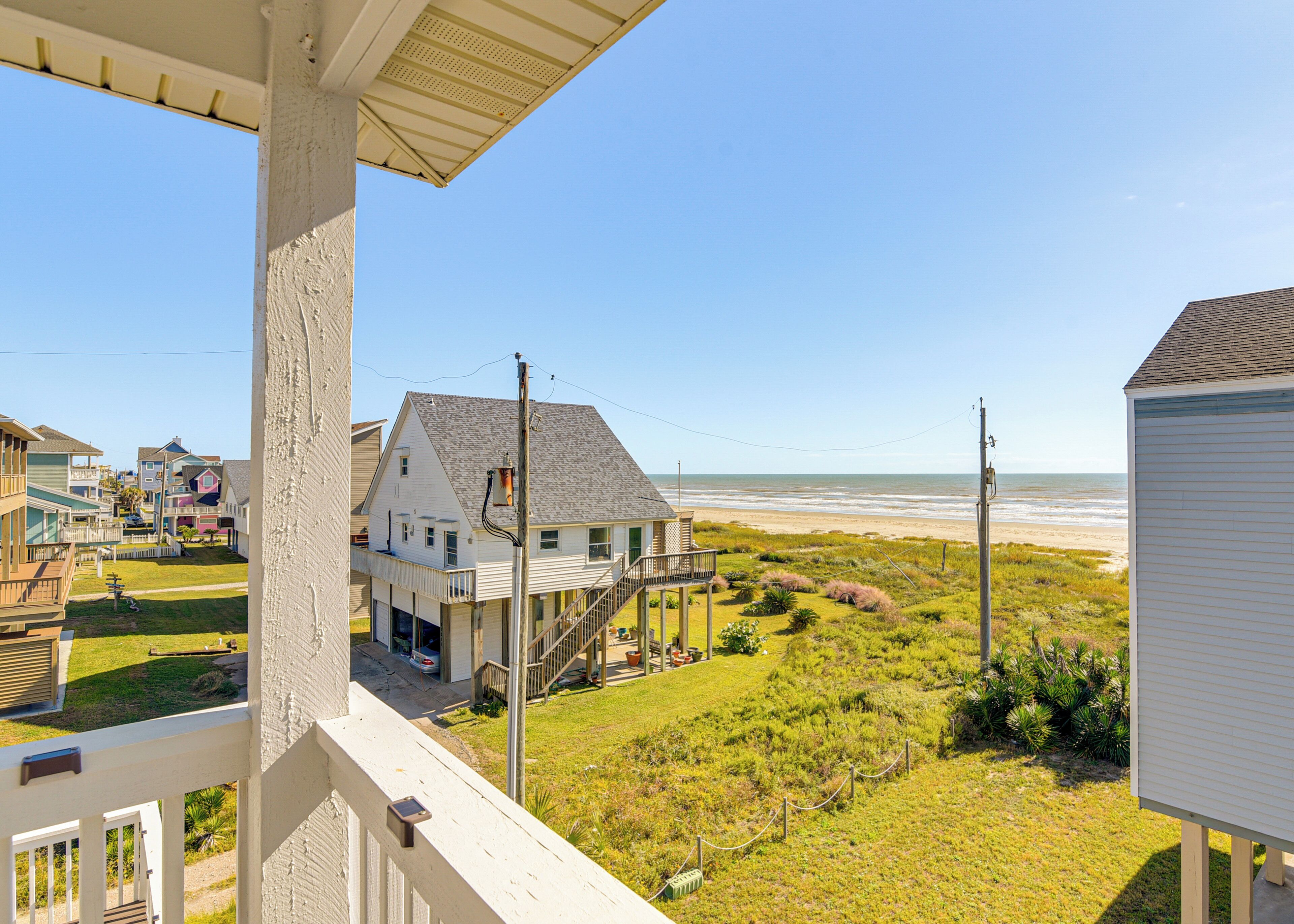 A coastal house with a balcony overlooking a beach.