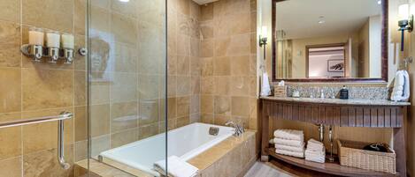 A modern bathroom with a glass-enclosed shower, a freestanding bathtub, and a vanity with a large mirror and towel storage.