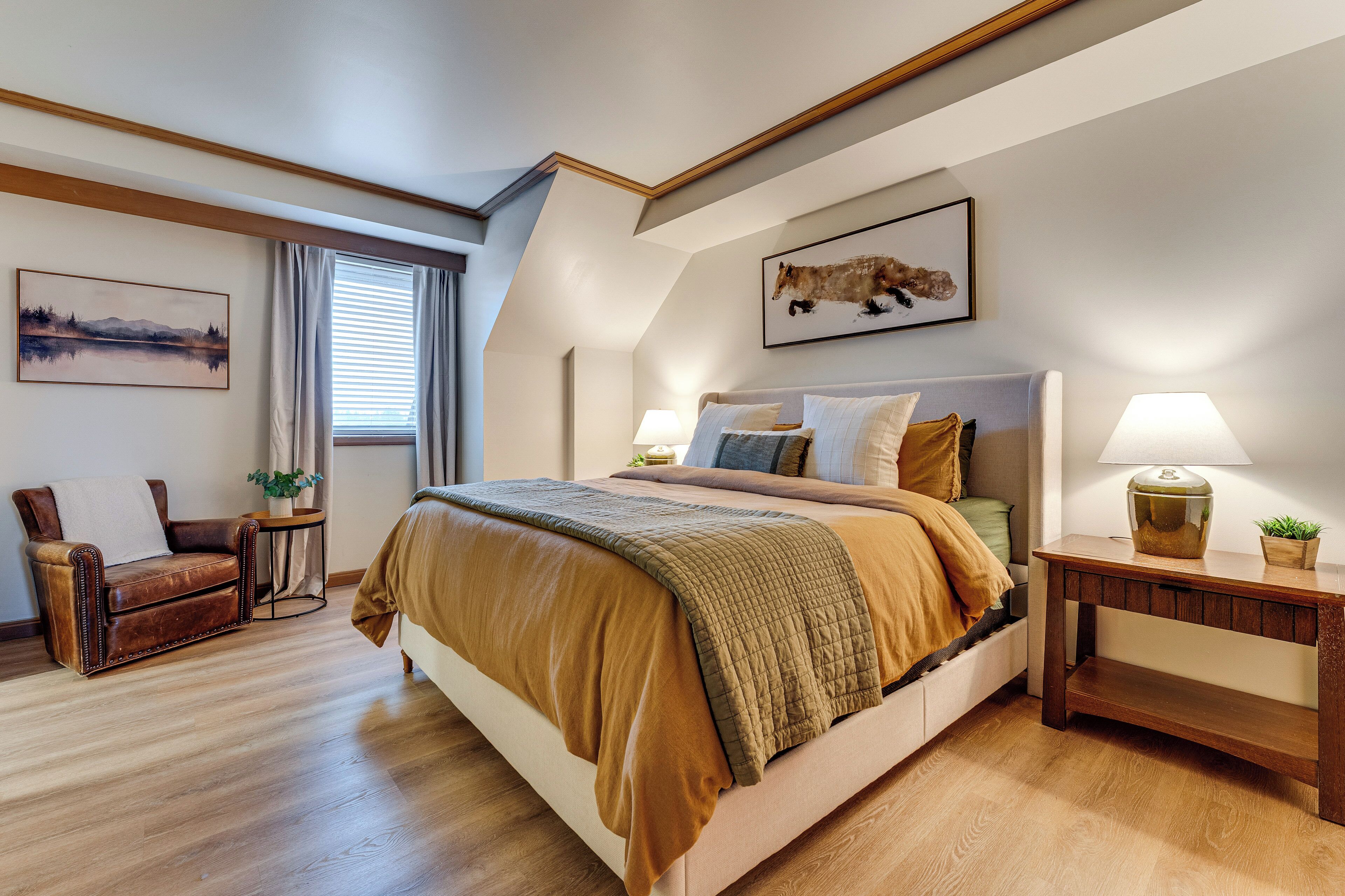 A bedroom with a large bed, a wooden floor, a sofa, a small table, and a painting on the wall.
