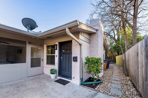 A house with a satellite dish, a black door, a small garden, and a gravel pathway. - Walk to UT Austin! Charming Duplex w/ Game Room (Austin)